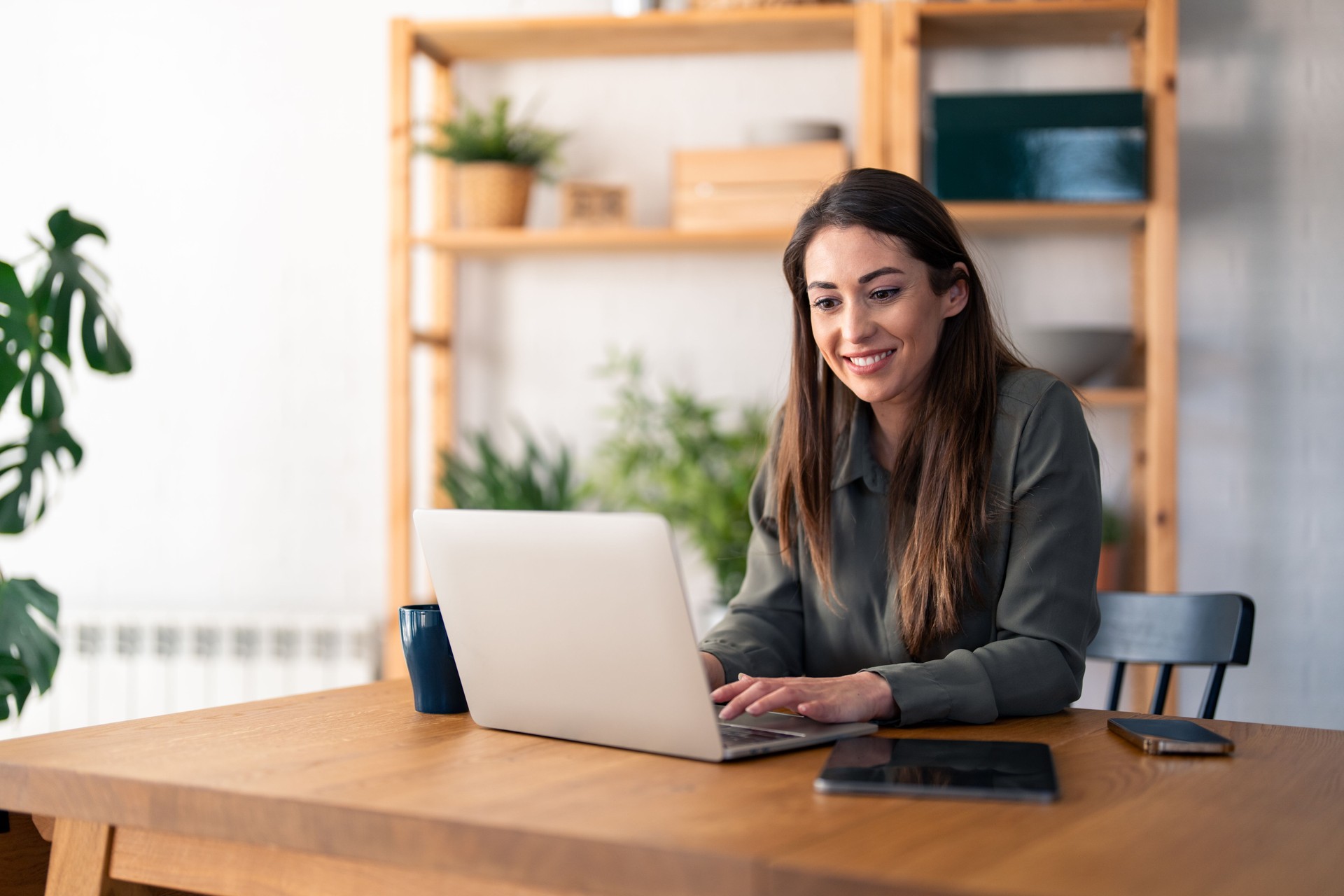 Satisfied beautiful millennial woman typing on laptop computer while sitting at table in home office